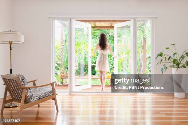 hispanic woman opening french doors to patio - french doors stockfoto's en -beelden