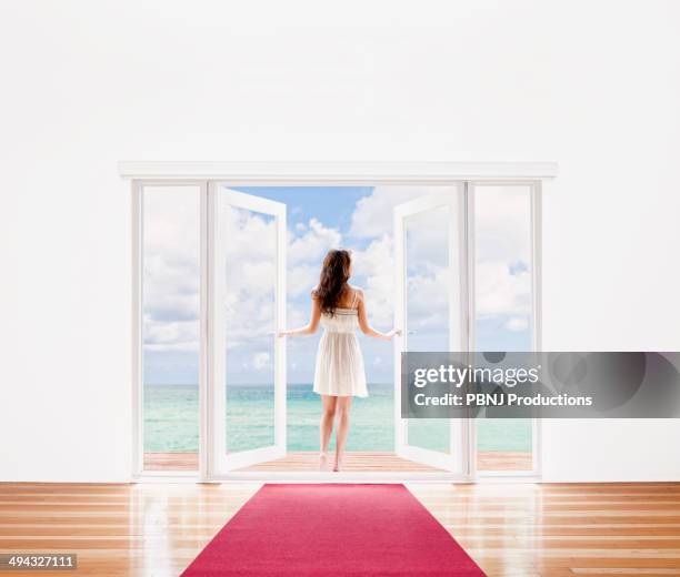 hispanic woman opening french doors to ocean view - barefoot female celebrities stock pictures, royalty-free photos & images