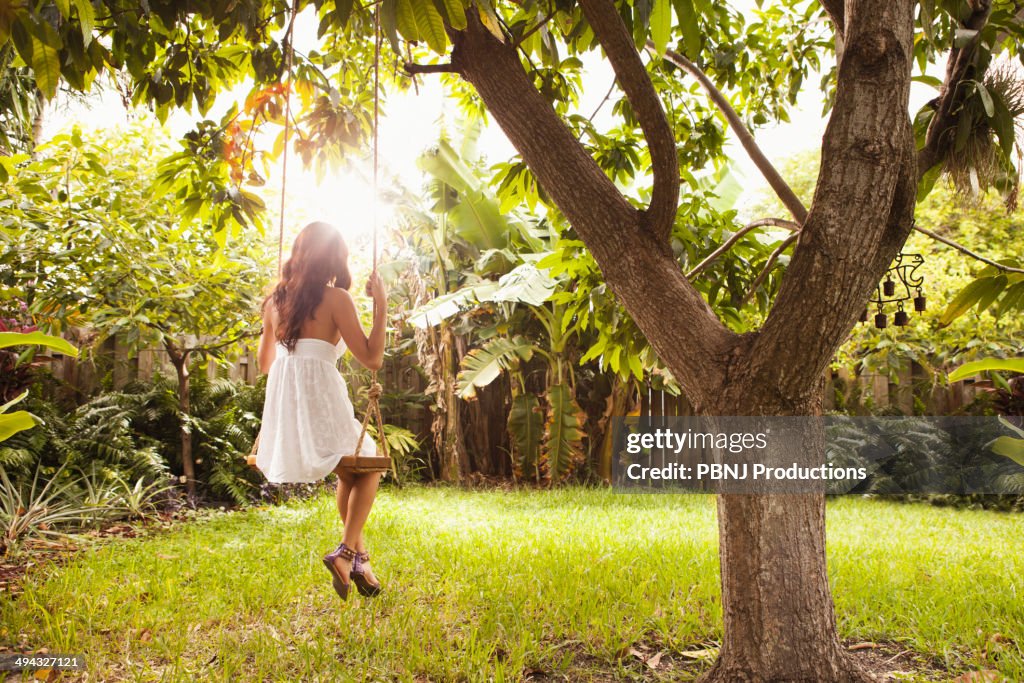 Hispanic woman sitting on tree swing