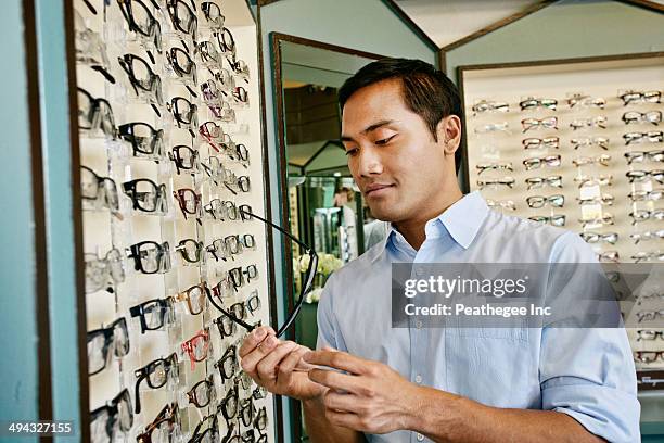 filipino man trying on glasses at optometrist - buying eyeglasses stock pictures, royalty-free photos & images