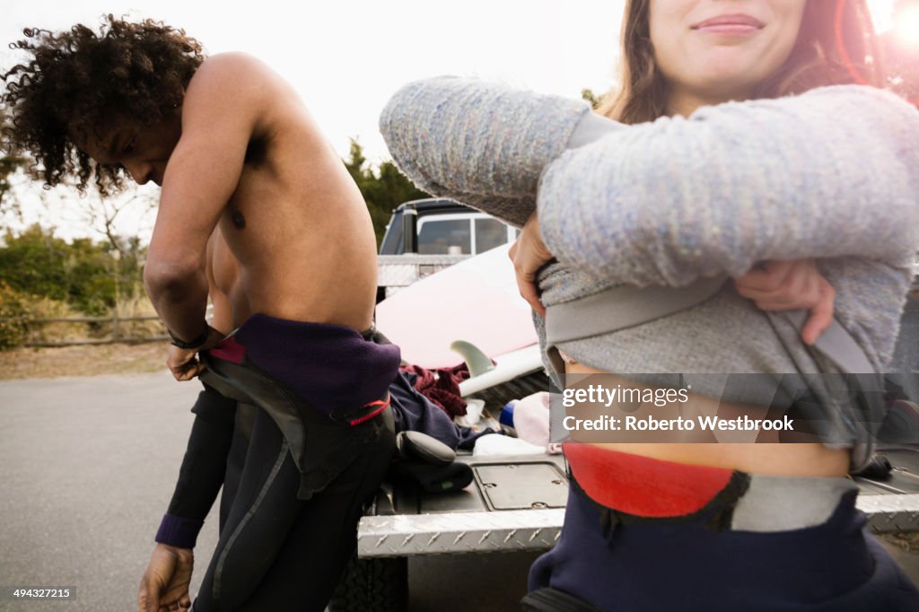 Surfers pulling on wet suits by truck