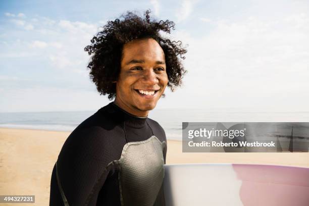 mixed race surfer carrying board on beach - native african ethnicity stock-fotos und bilder