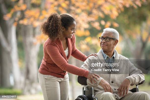african american woman pushing father in wheelchair - healthcare worker imagens e fotografias de stock