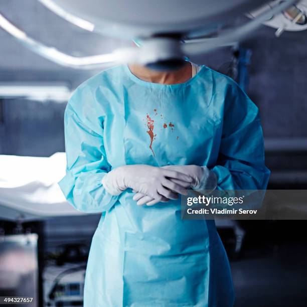 caucasian surgeon with blood on gown in operating room - gloves clasped hands ストックフォトと画像