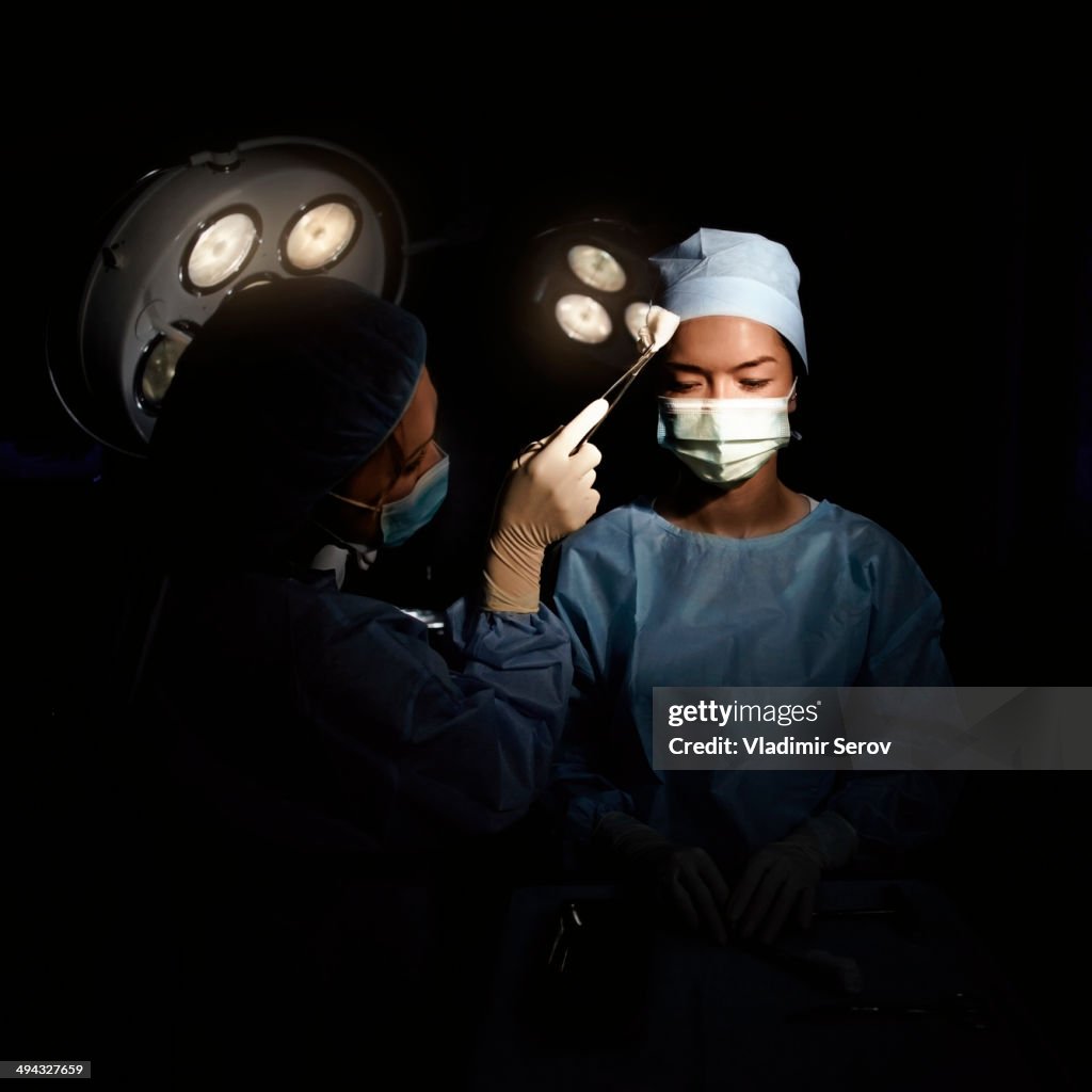 Caucasian nurse wiping sweat from surgeon's brow