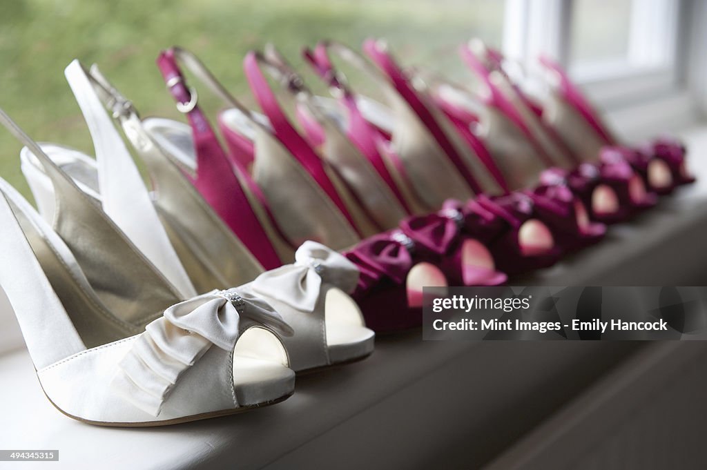 A row of high heeled shoes. Pairs of peep toe slingbacks in white and pink. Special occasion.