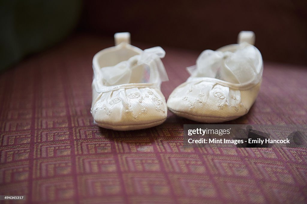 A pair of cream-coloured embroidered satin Christening boots with lace ribbon bows.