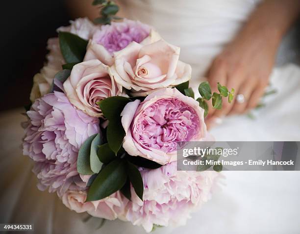 a woman, a bride holding a bridal bouquet of pastel coloured pale pink roses and peonies. - peonies bouquet stock pictures, royalty-free photos & images