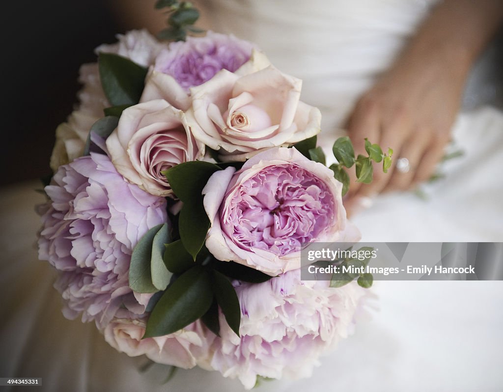 A woman, a bride holding a bridal bouquet of pastel coloured pale pink roses and peonies.