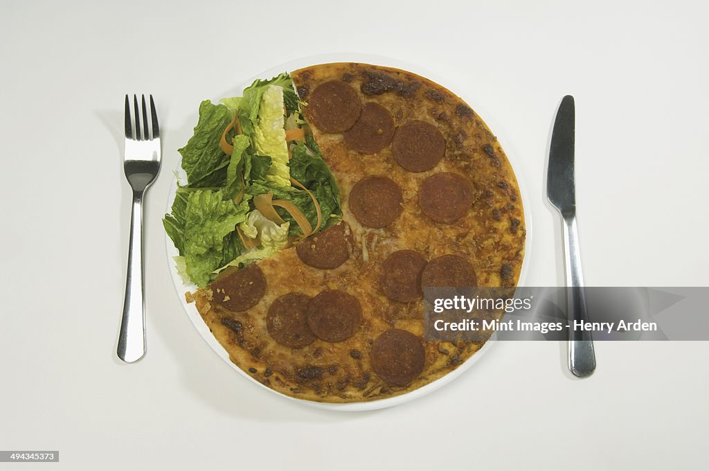 A salami pizza and salad on a plate.