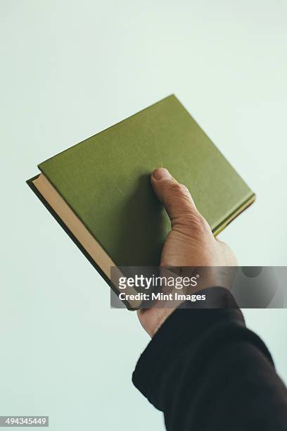 a man's hand holding an old green hardback book. - book sleeve stock pictures, royalty-free photos & images