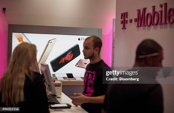 An advertisement for Apple Inc. IPhone is displayed as an employee, center, assists a customer at a T-Mobile US Inc. Store in New York, U.S., on...