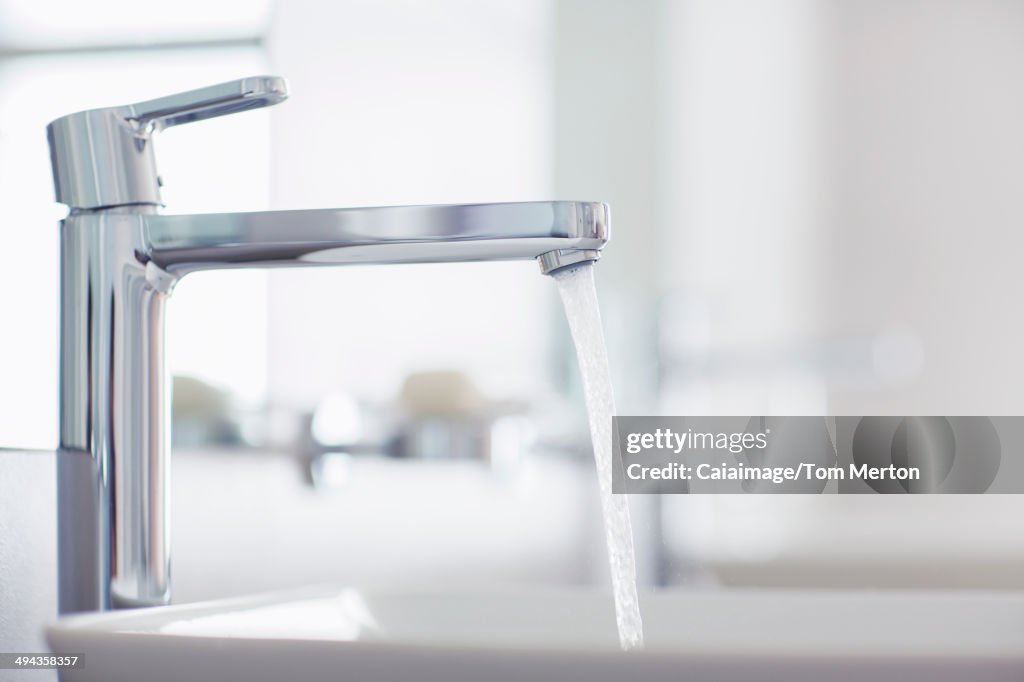 Water pouring from modern faucet in bathroom