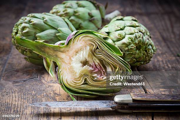 sliced and whole organic artichokes and kitchen knife on wooden table - artichoke stock pictures, royalty-free photos & images