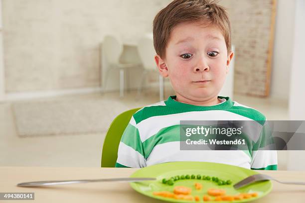 germany, munich , boy eating peas and carrots showing anthropomorphic face - surprise face kid stock-fotos und bilder
