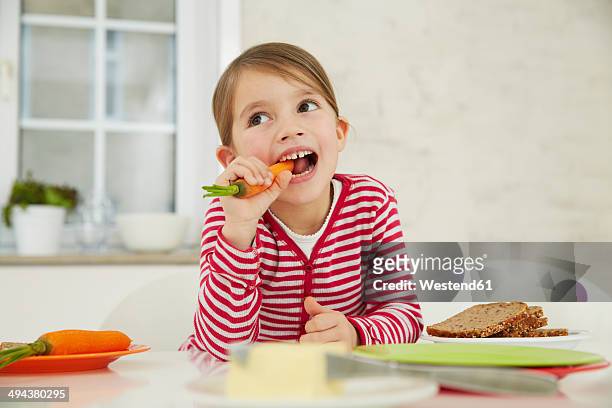 germany, munich, girl sitting at table with bunch of carrots on head - diet carrot stock-fotos und bilder