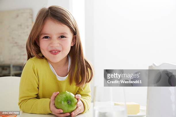 germany, munich, girl sitting at table with green apple - child holding apples stock-fotos und bilder