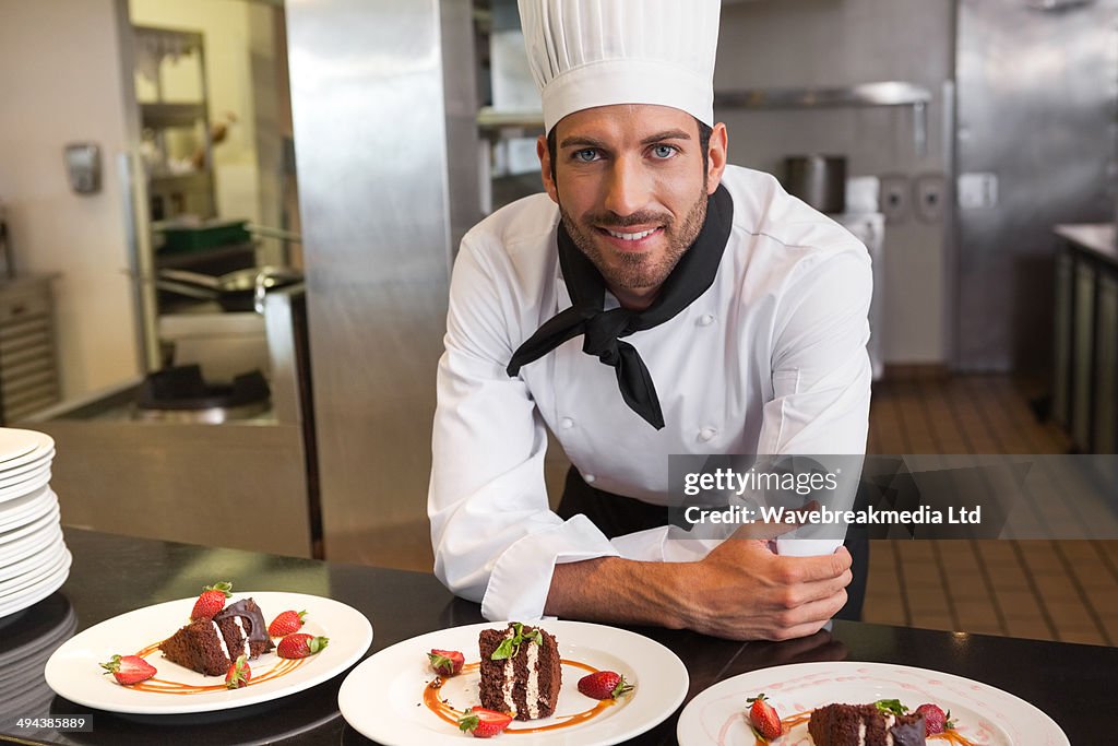 Happy chef looking at camera behind counter of desserts