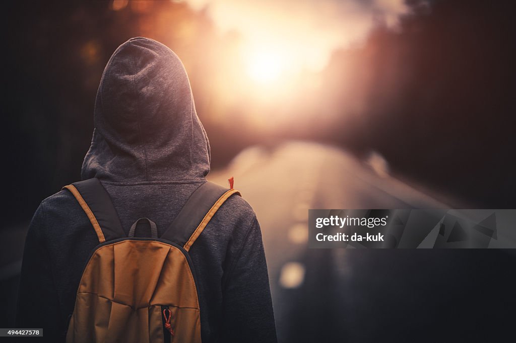 Traveler with backpack walking forward alone at sunset