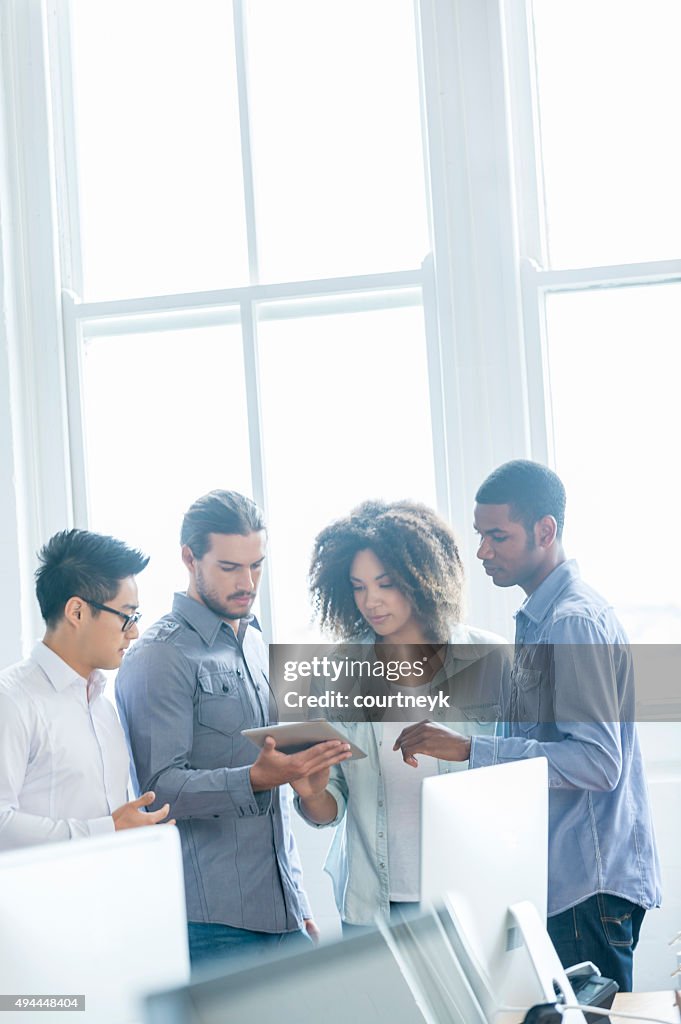 4 people working on a digital tablet in an office.