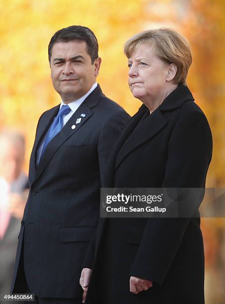 German Chancellor Angela Merkel and Honduran President Juan Orlando Hernandez listen to their countries' respective national anthems upon Hernandez's...