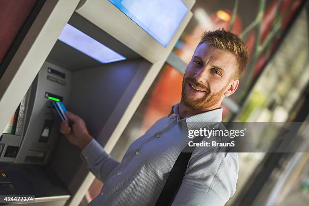 young happy businessman removing cash from atm. - man atm smile stock pictures, royalty-free photos & images