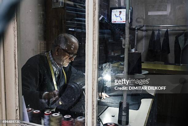 Tailor works in his workshop in downtown Istanbul on October 27 as the television set in background displays a live broadcast of the Turkish prime...