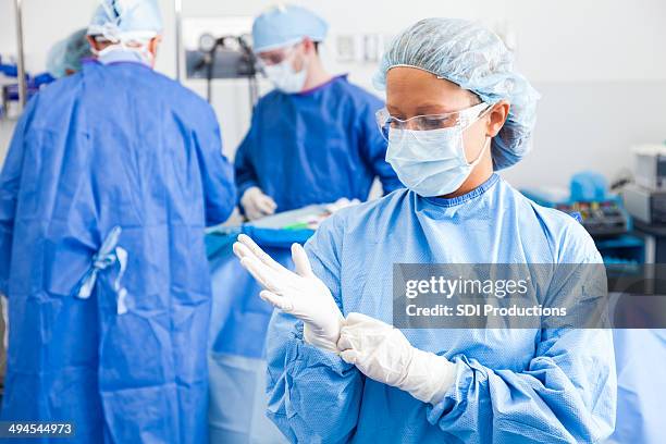female surgeon putting on surgical gloves before performing operation - operatiegewaad stockfoto's en -beelden