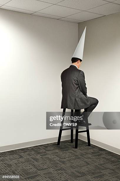 businessman sitting in office corner wearing dunce cap - dumstrut bildbanksfoton och bilder