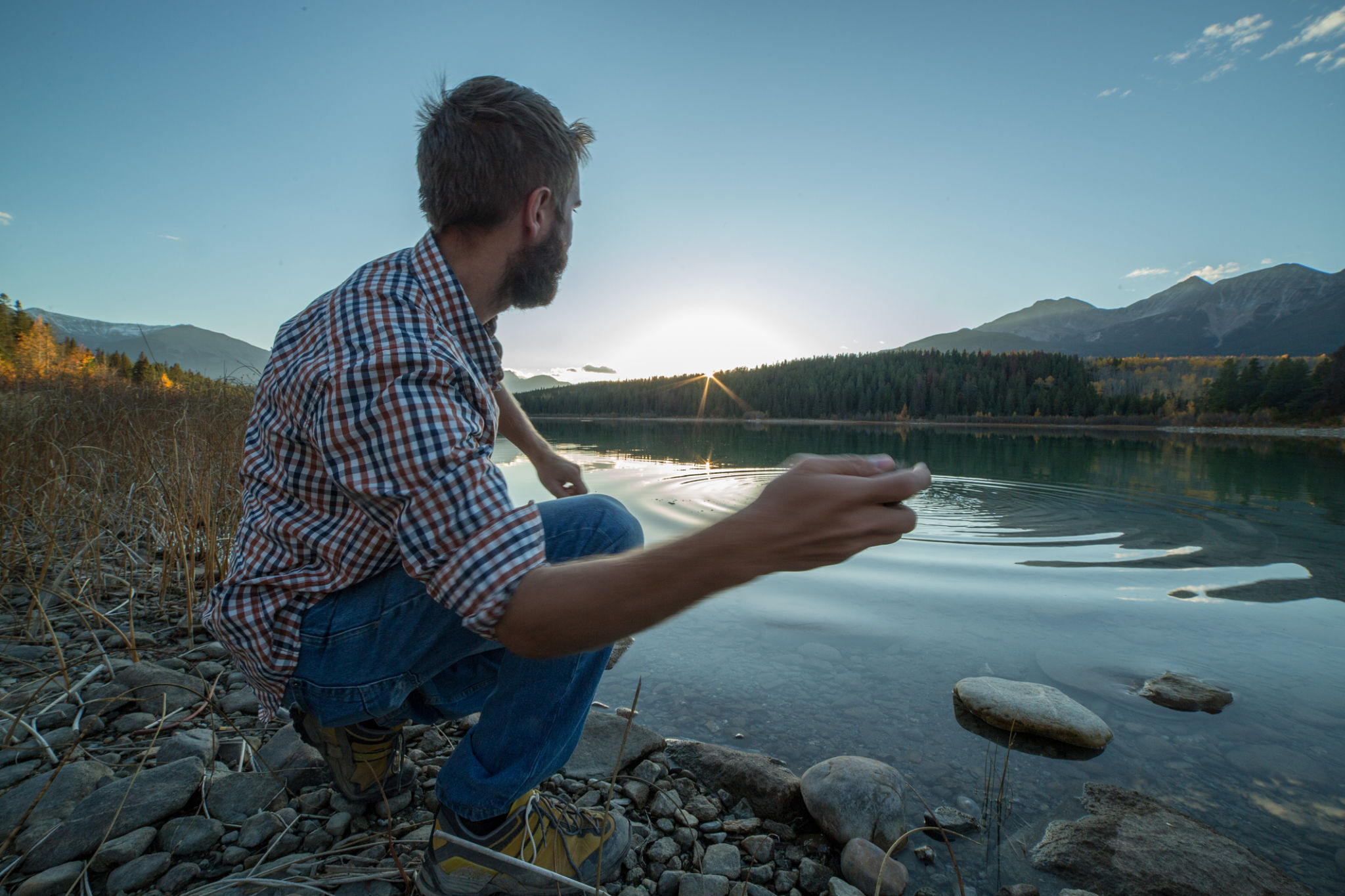 Young man by the lake at sunset skimming stones Young man by the lake at sunset skimming stones