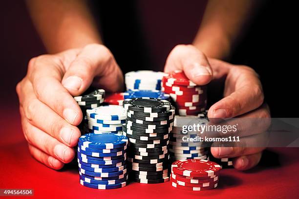 Man"s hands move the winnings casino chips on red table.
