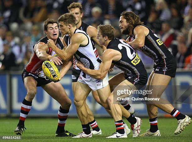 Josh Thomas of the Magpies handballs whilst being tackled by Tom Curren of the Saints during the round 11 AFL match between the St Kilda Saints and...