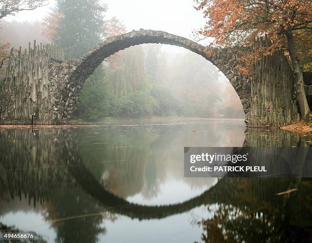 Fog hangs over trees in autumnal colors and the so-called Rakotzbruecke bridge of the Rhododendronpark Kromlau landscaped park in Kromlau, eastern...