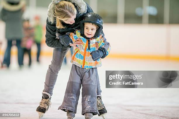 madre aiutando suo figlio imparare a pattinare sul ghiaccio - pista di pattinaggio su ghiaccio foto e immagini stock