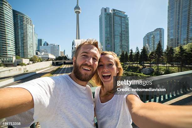 young cheerful couple in toronto taking selfie portrait with cityscape - toronto summer stock pictures, royalty-free photos & images