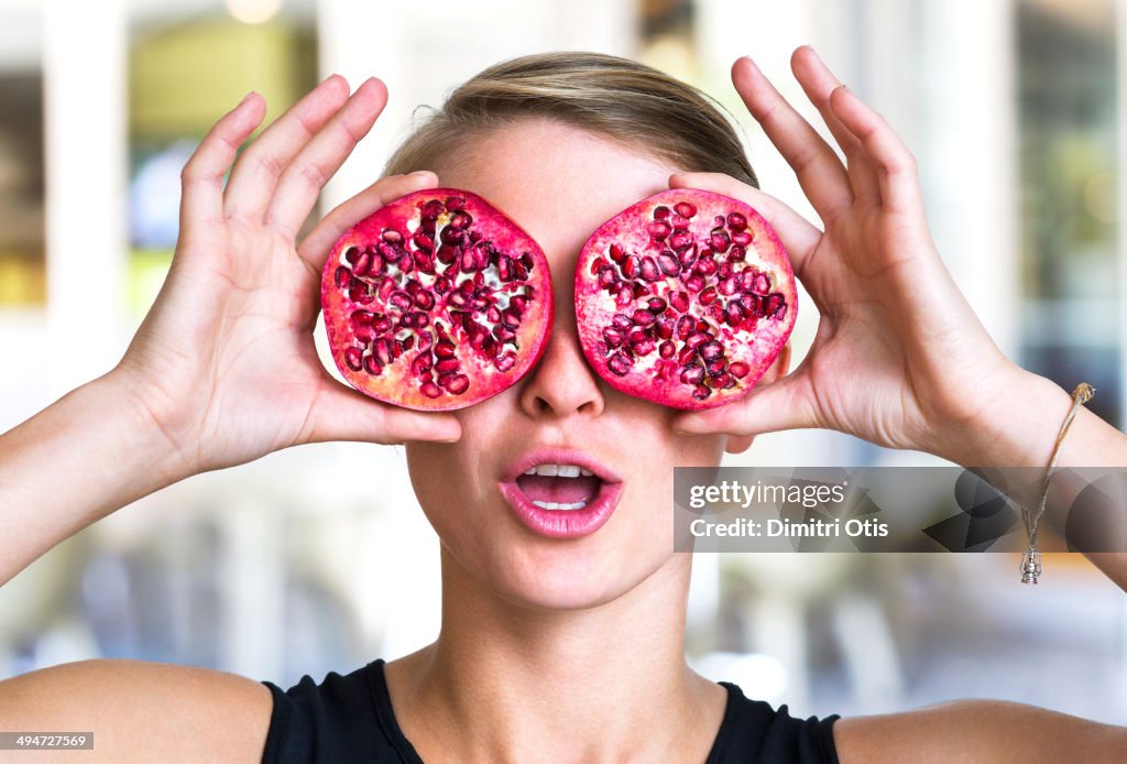 Young woman holding pomegranate slices as glasses