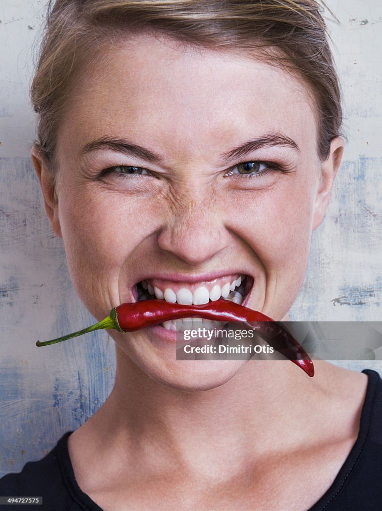 Young woman biting red hot chilli