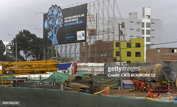 Construction workers go about their chores at a site in Lima on May 30, 2014 near a billboard that filters pollution from the air and is capable of...