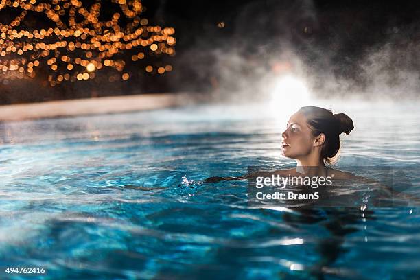 young woman enjoying in a heated swimming pool at night. - spa behandeling stockfoto's en -beelden
