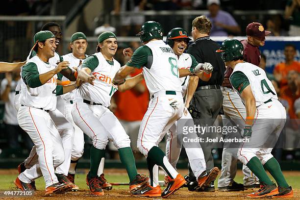 David Thompson of the Miami Hurricanes is congratulated by teammates after scoring the winning run on a wild pitch by Scott Garner of the...