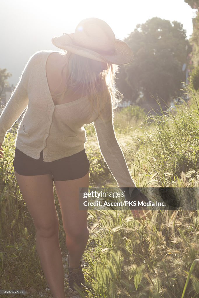 Young woman strokes grasses at edge of trail