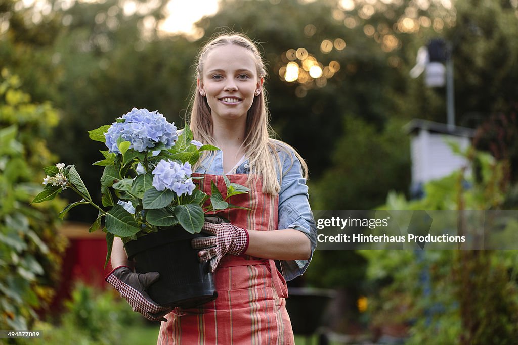 Young Woman With Plant Standing In Garden