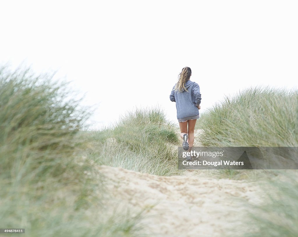 Woman running in sand dunes at beach.