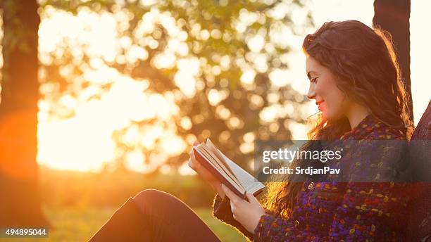 relajarse con un buen libro - mujer leyendo libro en el parque fotografías e imágenes de stock