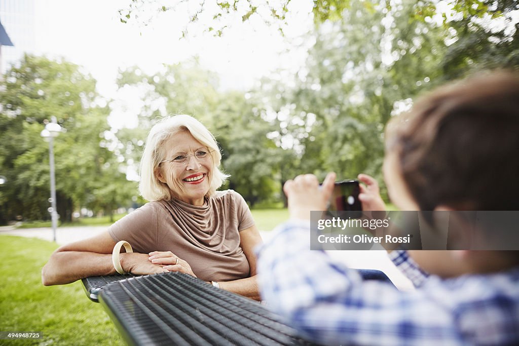 Boy taking picture of grandmother on park bench