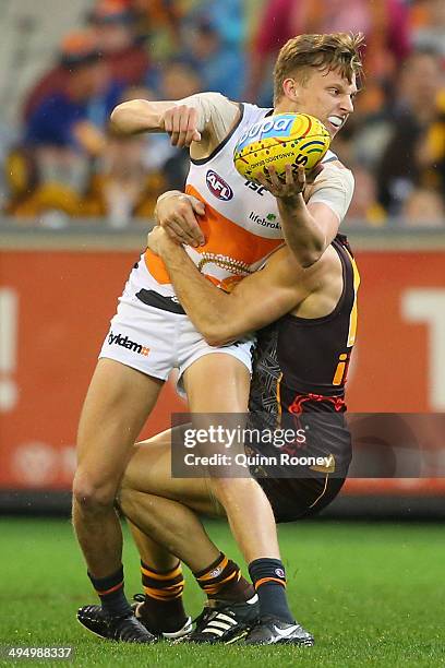 Lachie Whitfield of the Giants handballs whilst being tackled by Paul Puopolo of the Hawks during the round 11 AFL match between the Hawthorn Hawks...