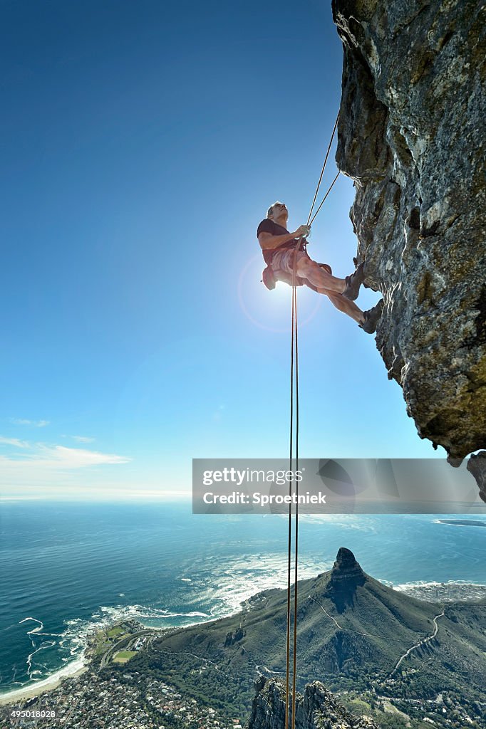 Abseiling climber over precipice looks up at rock face