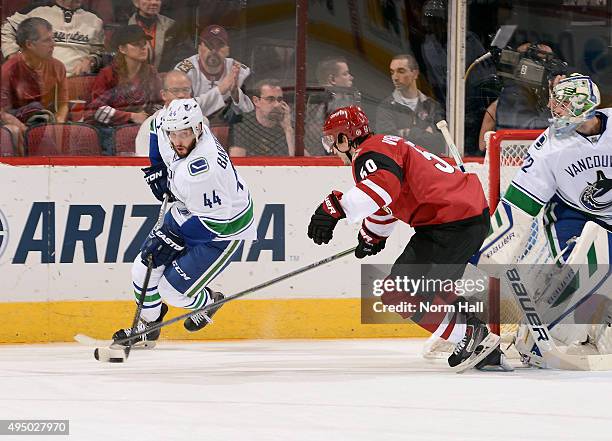 Matt Bartkowski of the Vancouver Canucks advance the puck around goaltender Richard Bachman as Antoine Vermette of the Arizona Coyotes skates in...