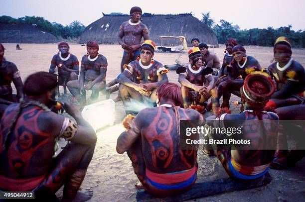 Body-painted indigenous men gather around a solar powered electric torch, Xingu National park, Amazon rainforest, Brazil.