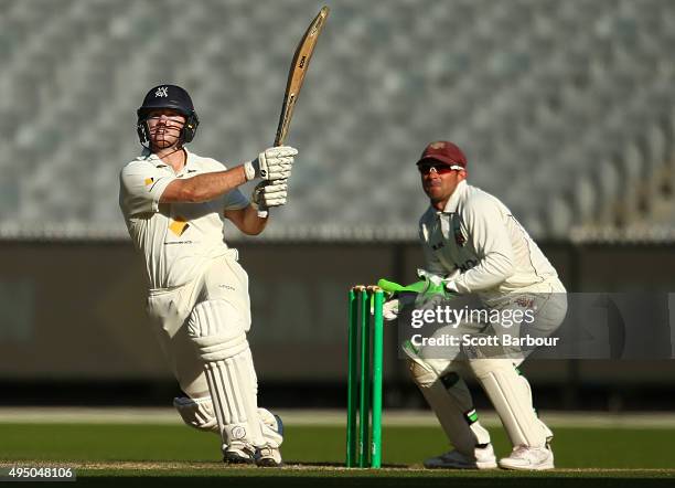 Travis Dean of Victoria hits a boundary to bring up his century as wicketkeeper Chris Hartley of Queensland looks on during day four of the Sheffield...